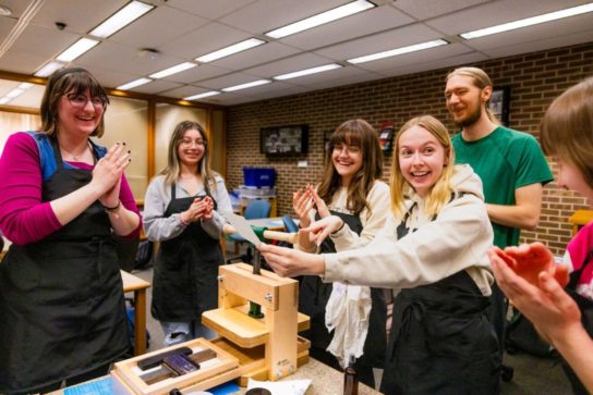 Rachael Manning (far left) cheers with other students after her classmate created a print during the Technologies of the Word course in NIU’s BookLab this spring.