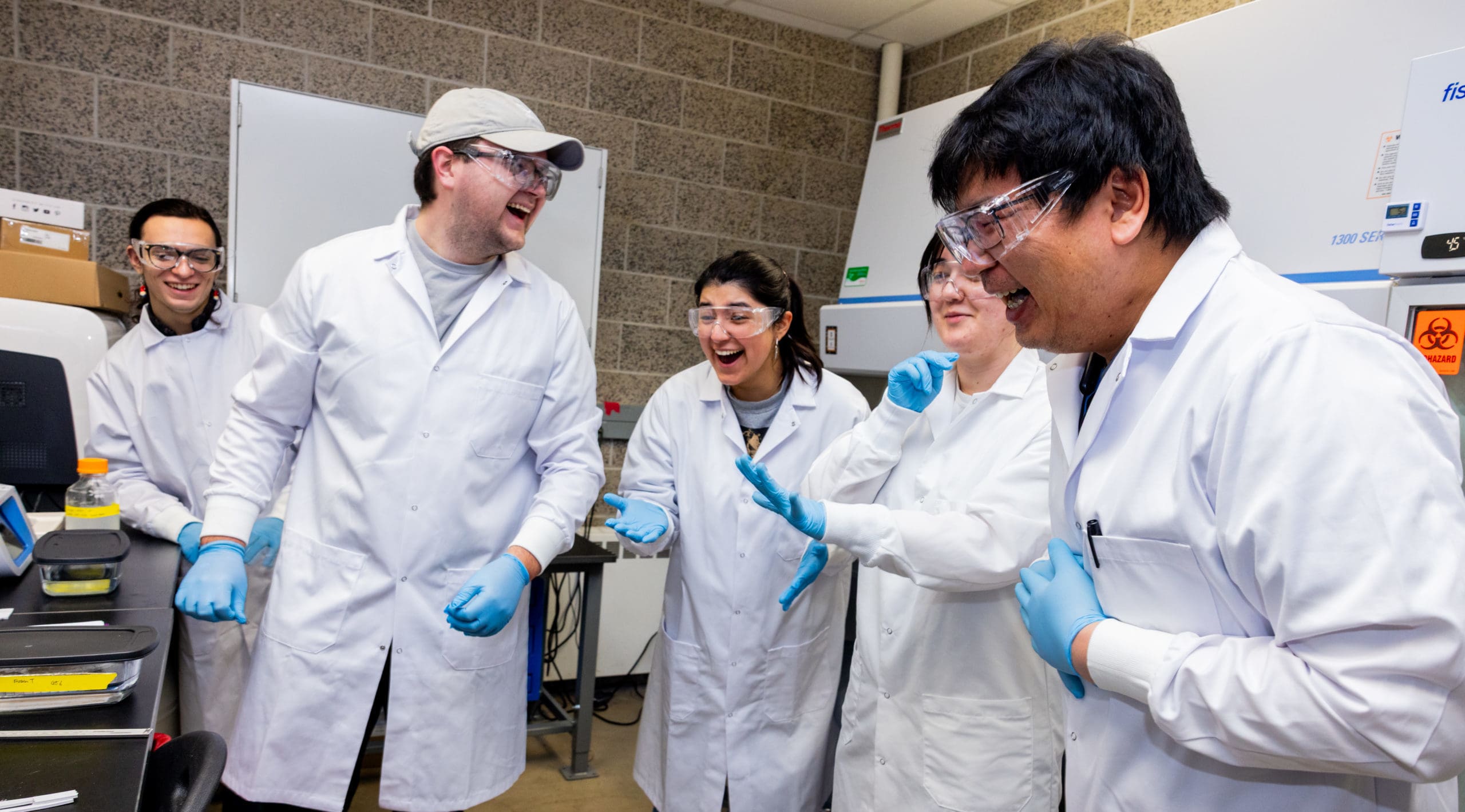 NIU classmates in a lab with lab coats and PPE and laughing together