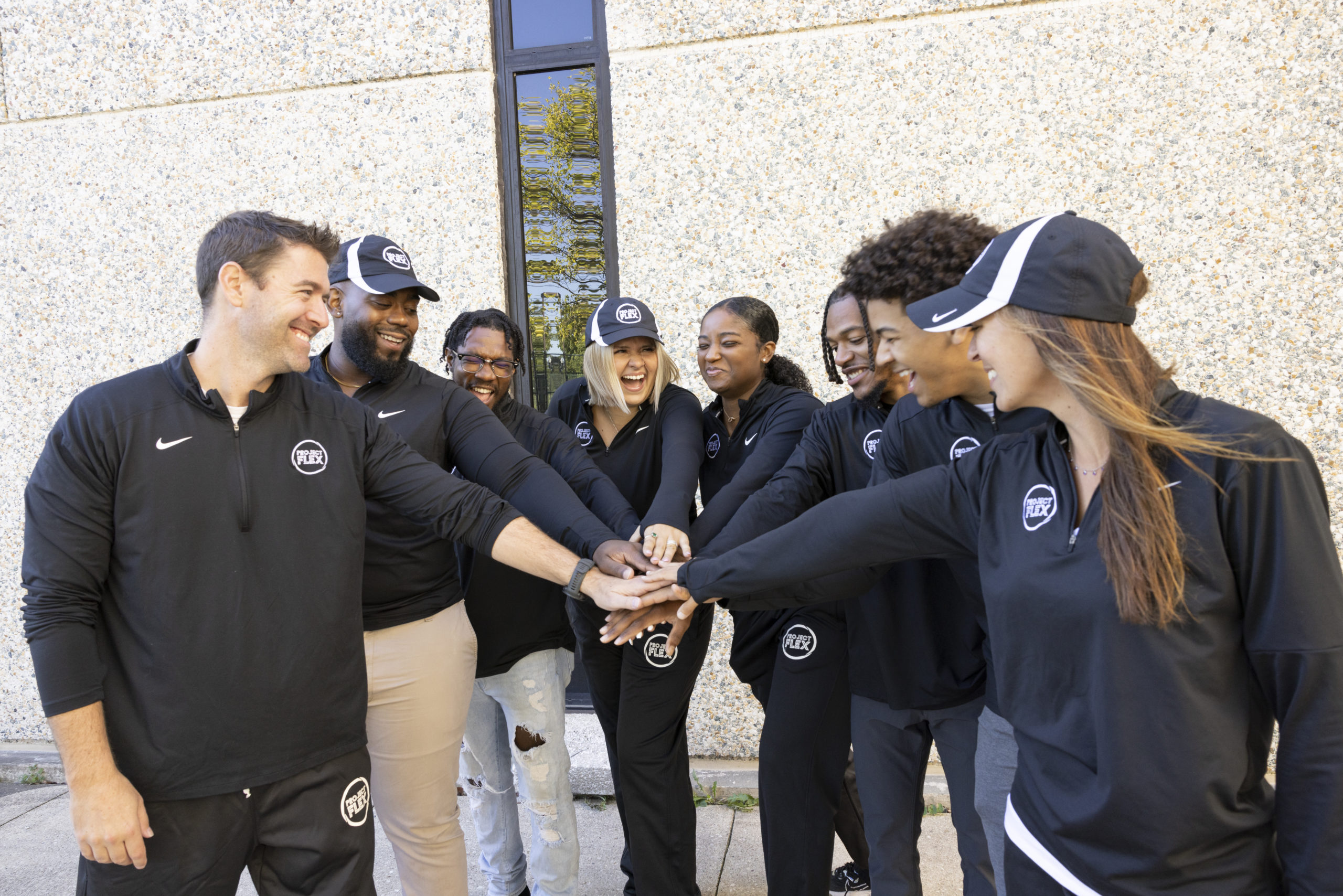 Diverse group of smiling NIU students putting their hands together in a circle.