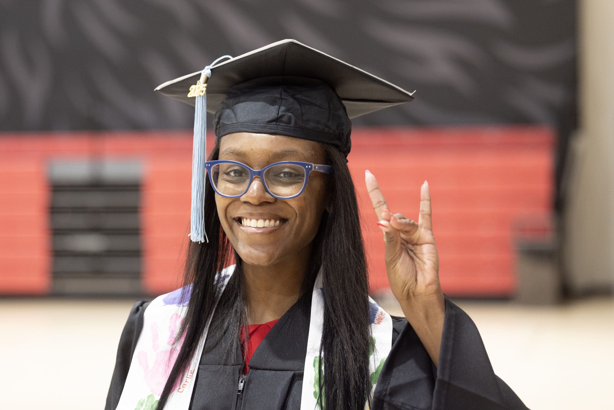 Smiling Black female NIU student in graduation cap and gown making a Huskie hand sign.